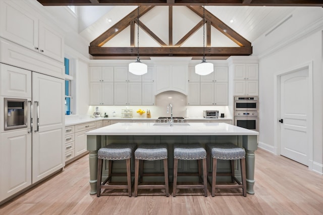 kitchen featuring hanging light fixtures, an island with sink, a breakfast bar area, and white cabinetry