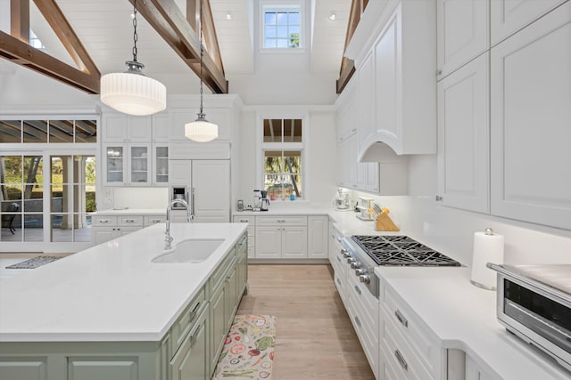 kitchen featuring sink, an island with sink, pendant lighting, stainless steel gas stovetop, and white cabinets