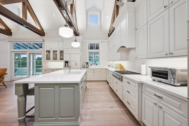 kitchen with decorative light fixtures, stainless steel gas stovetop, white cabinetry, sink, and a kitchen island with sink