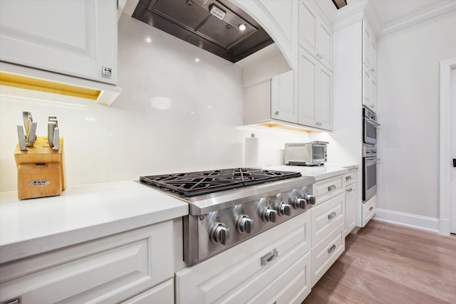 kitchen with stainless steel appliances, white cabinetry, wall chimney range hood, and light hardwood / wood-style flooring