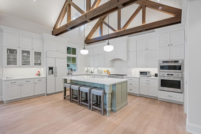 kitchen featuring appliances with stainless steel finishes, decorative light fixtures, white cabinetry, sink, and a kitchen island with sink