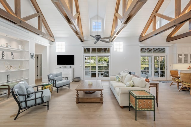 living room with built in shelves, light hardwood / wood-style flooring, ceiling fan, beamed ceiling, and a towering ceiling