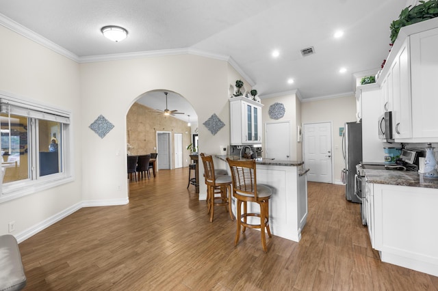 kitchen with crown molding, appliances with stainless steel finishes, white cabinetry, dark stone countertops, and kitchen peninsula