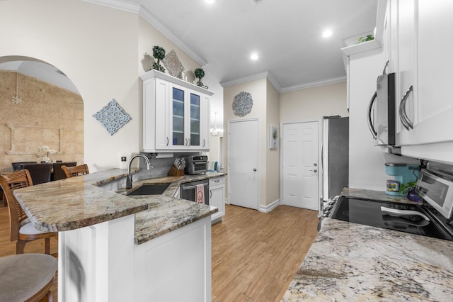 kitchen with a kitchen bar, ornamental molding, kitchen peninsula, stone counters, and white cabinets