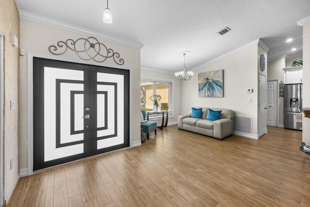 foyer entrance with french doors, a chandelier, a textured ceiling, light wood-type flooring, and ornamental molding