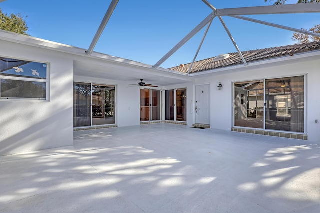 back of property with stucco siding, a ceiling fan, glass enclosure, and a patio area