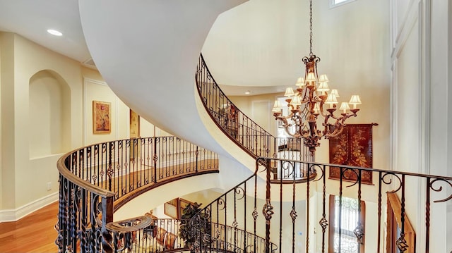 stairway featuring recessed lighting, wood finished floors, a towering ceiling, baseboards, and an inviting chandelier