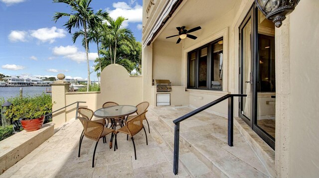 view of patio / terrace with a water view, an outdoor kitchen, outdoor dining space, a grill, and ceiling fan