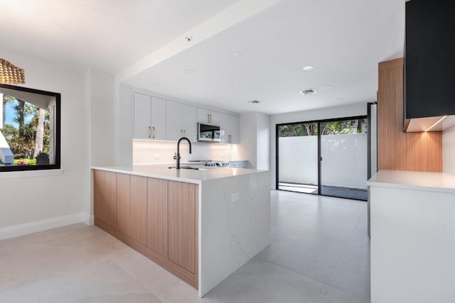 kitchen featuring white cabinetry, kitchen peninsula, sink, and tasteful backsplash