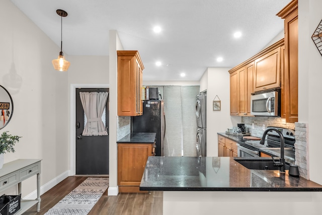 kitchen with pendant lighting, stainless steel appliances, tasteful backsplash, kitchen peninsula, and stacked washing maching and dryer