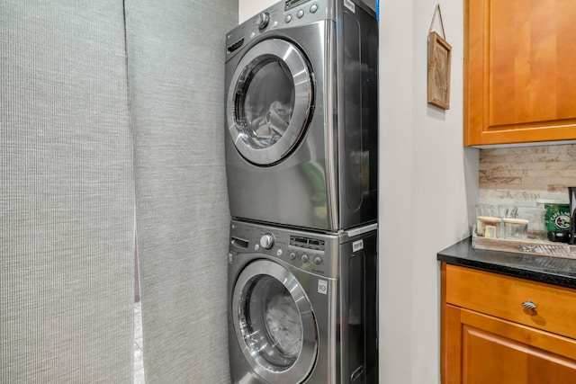 clothes washing area with stacked washing maching and dryer and cabinets