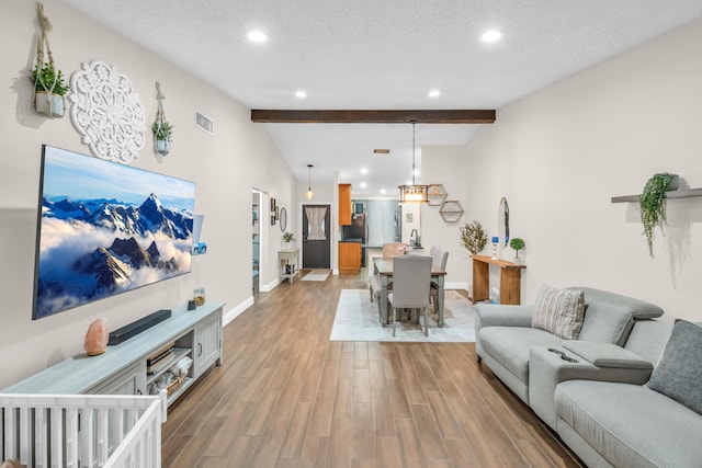 living room featuring sink, vaulted ceiling with beams, light hardwood / wood-style floors, and a textured ceiling