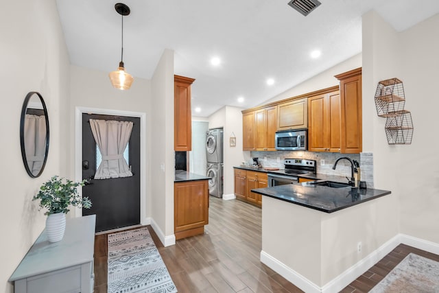 kitchen featuring decorative light fixtures, stainless steel appliances, sink, stacked washing maching and dryer, and kitchen peninsula