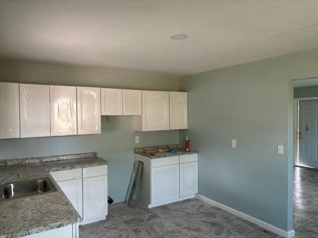 kitchen featuring white cabinets, light stone countertops, and sink