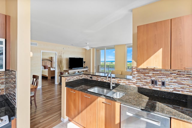 kitchen featuring stainless steel dishwasher, dark stone counters, sink, and decorative backsplash