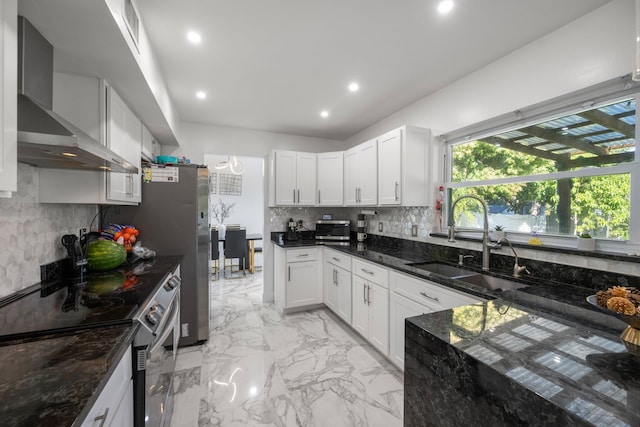 kitchen with sink, dark stone countertops, appliances with stainless steel finishes, wall chimney range hood, and white cabinets