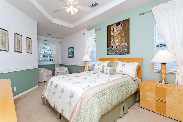 bedroom with ceiling fan, a tray ceiling, and light carpet