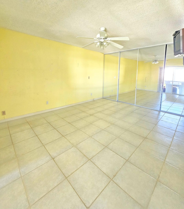 empty room with baseboards, light tile patterned floors, a textured ceiling, and ceiling fan