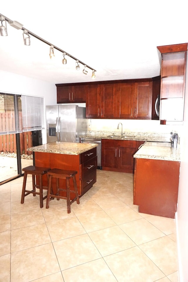 kitchen featuring a center island, stainless steel appliances, sink, light stone counters, and light tile patterned floors