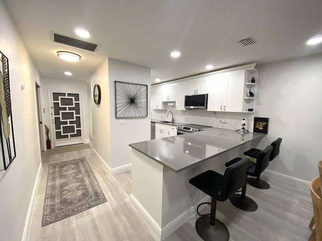 kitchen featuring appliances with stainless steel finishes, white cabinetry, kitchen peninsula, a breakfast bar, and light hardwood / wood-style flooring