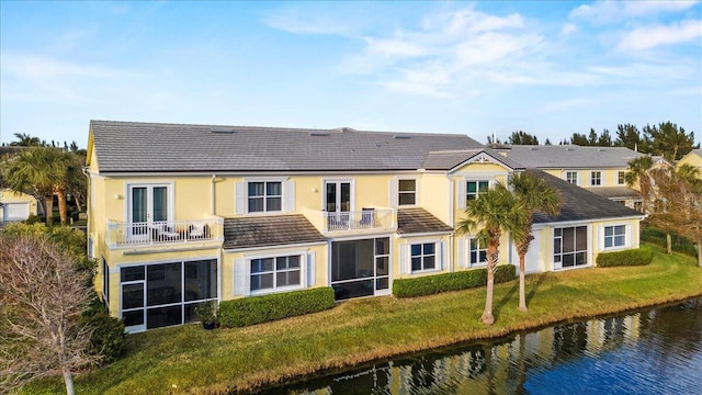 rear view of house featuring a water view, a balcony, a sunroom, and a lawn