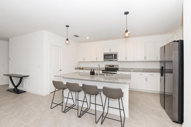 kitchen with pendant lighting, stainless steel appliances, a center island with sink, and white cabinets