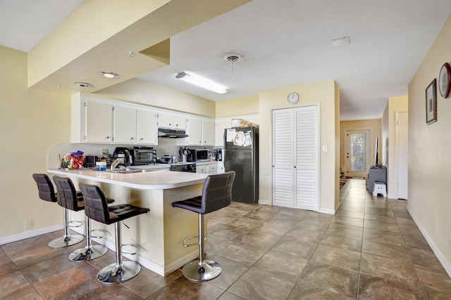 kitchen featuring black refrigerator, white cabinetry, electric range, a kitchen bar, and kitchen peninsula