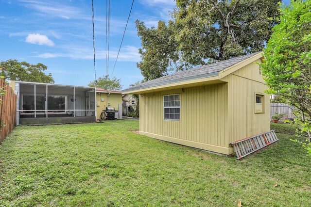 back of property with an outbuilding, a sunroom, and a lawn