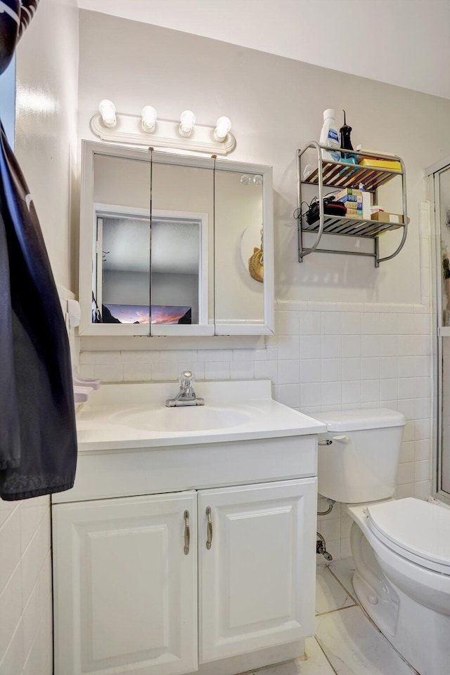 bathroom featuring a shower with shower door, tile walls, vanity, toilet, and tile patterned floors