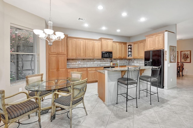 kitchen featuring decorative light fixtures, light stone counters, a kitchen bar, an island with sink, and black appliances