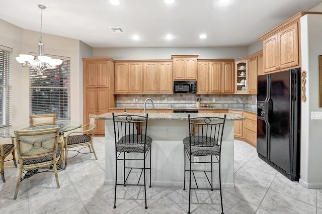 kitchen featuring black appliances, a kitchen bar, tasteful backsplash, light stone counters, and a center island with sink