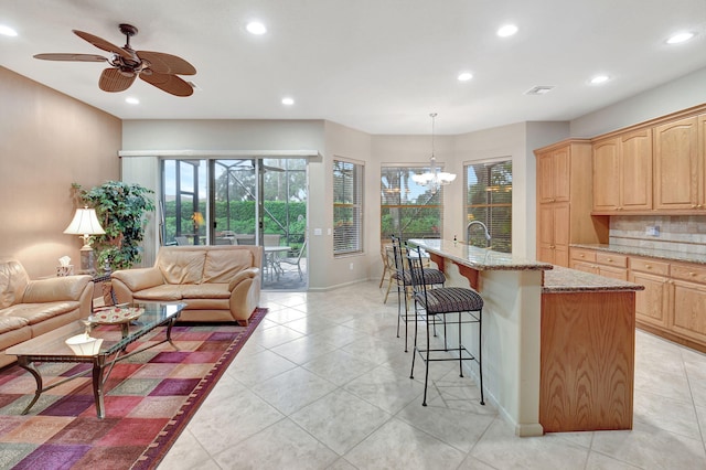 kitchen with a kitchen breakfast bar, hanging light fixtures, light stone counters, a center island with sink, and decorative backsplash