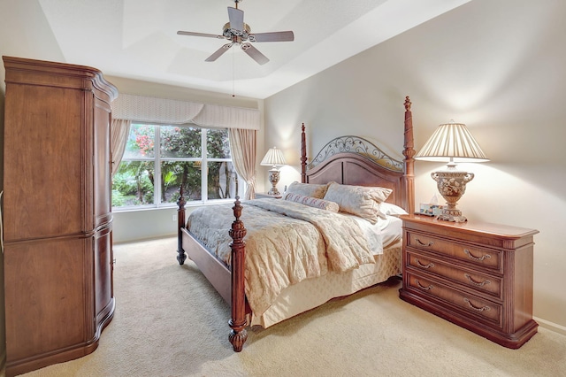 bedroom with ceiling fan, a tray ceiling, and light carpet