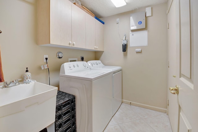 laundry area featuring a textured ceiling, sink, washing machine and dryer, cabinets, and light tile patterned flooring