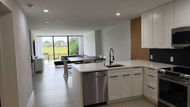 kitchen featuring appliances with stainless steel finishes, white cabinetry, a wall of windows, sink, and kitchen peninsula