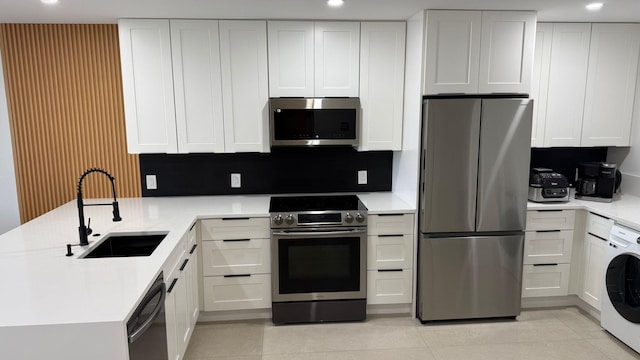 kitchen featuring appliances with stainless steel finishes, sink, washer / dryer, and white cabinetry