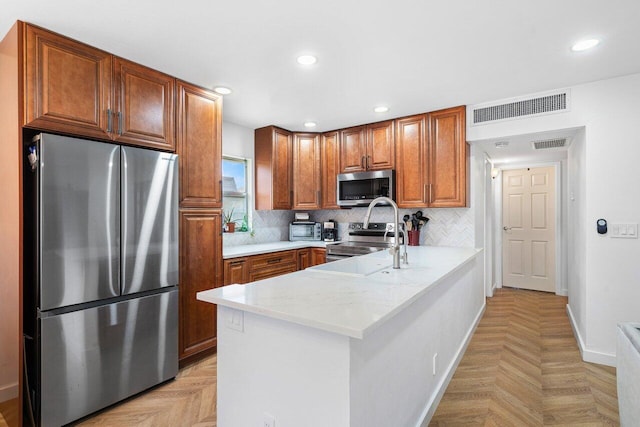 kitchen featuring light parquet floors, kitchen peninsula, stainless steel appliances, backsplash, and light stone countertops