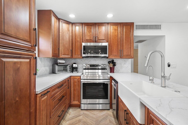 kitchen featuring light parquet floors, appliances with stainless steel finishes, decorative backsplash, light stone countertops, and sink