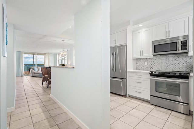 kitchen featuring appliances with stainless steel finishes, white cabinets, an inviting chandelier, backsplash, and light tile patterned flooring