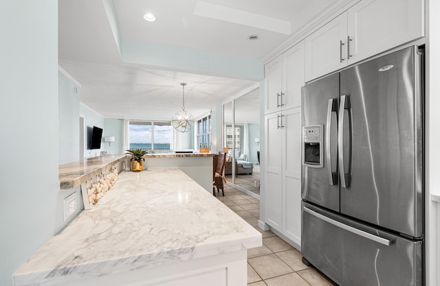 kitchen featuring pendant lighting, stainless steel fridge, white cabinetry, light tile patterned floors, and light stone countertops