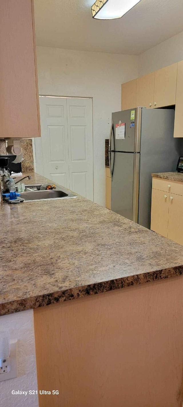 kitchen featuring decorative backsplash, sink, stainless steel fridge, and cream cabinetry