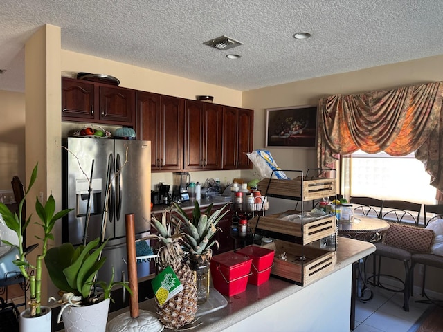 kitchen with dark brown cabinetry, light tile patterned flooring, a textured ceiling, and stainless steel fridge with ice dispenser