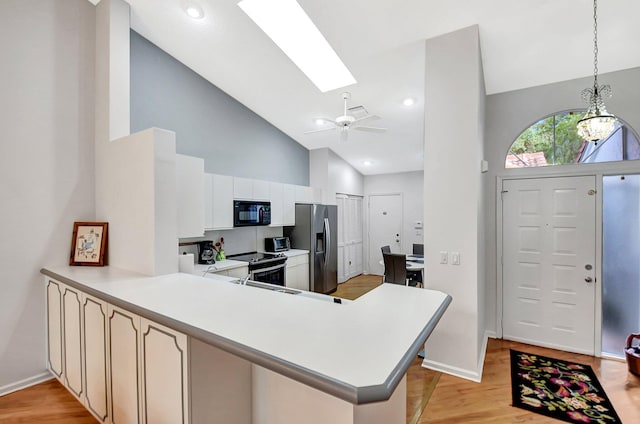 kitchen with a skylight, appliances with stainless steel finishes, kitchen peninsula, pendant lighting, and white cabinets