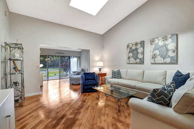 living area with high vaulted ceiling, a skylight, baseboards, and wood finished floors