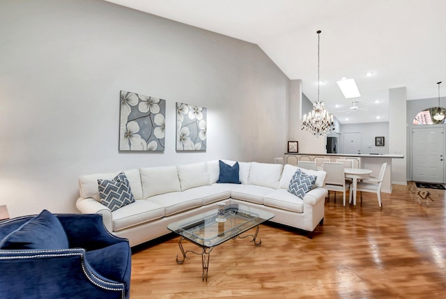 living room with light wood finished floors, baseboards, a chandelier, a skylight, and high vaulted ceiling