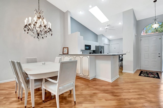 dining space with ceiling fan, high vaulted ceiling, a skylight, and light hardwood / wood-style floors