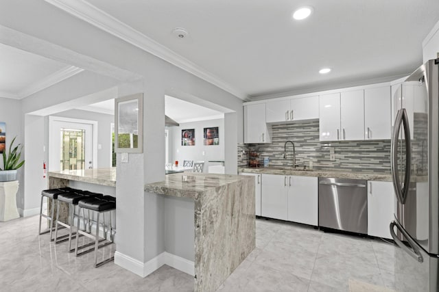 kitchen featuring sink, a breakfast bar area, appliances with stainless steel finishes, light stone counters, and white cabinets