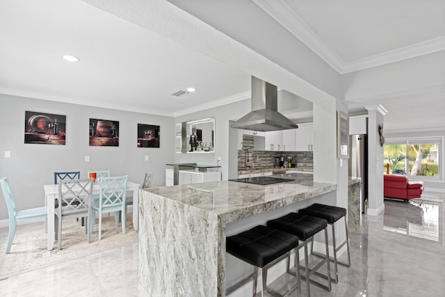 kitchen featuring island range hood, a breakfast bar area, white cabinets, crown molding, and light stone countertops