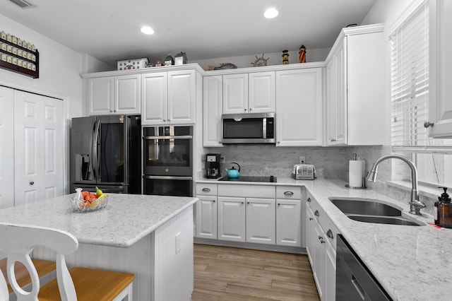 kitchen with sink, a breakfast bar area, white cabinets, black appliances, and light stone countertops