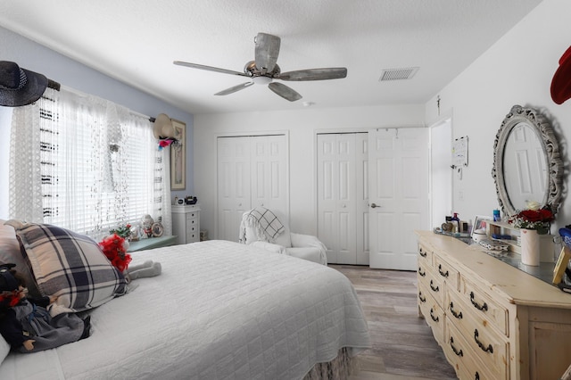 bedroom featuring ceiling fan, a textured ceiling, light hardwood / wood-style flooring, and two closets